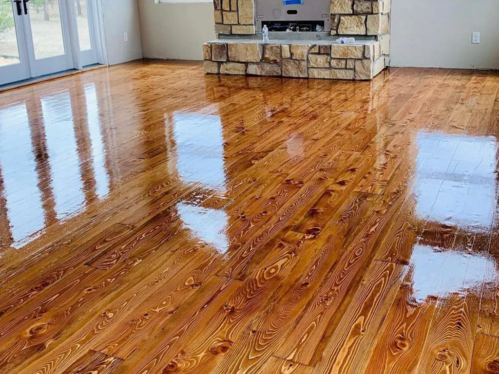 Glossy amber pine floor in a great room with a stone fireplace