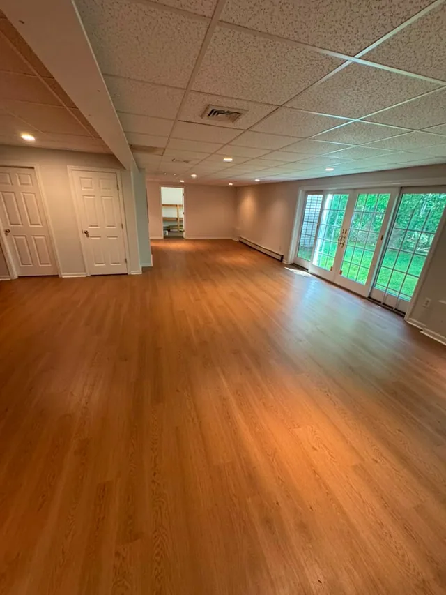 Warm-toned plank flooring in a large basement with French doors